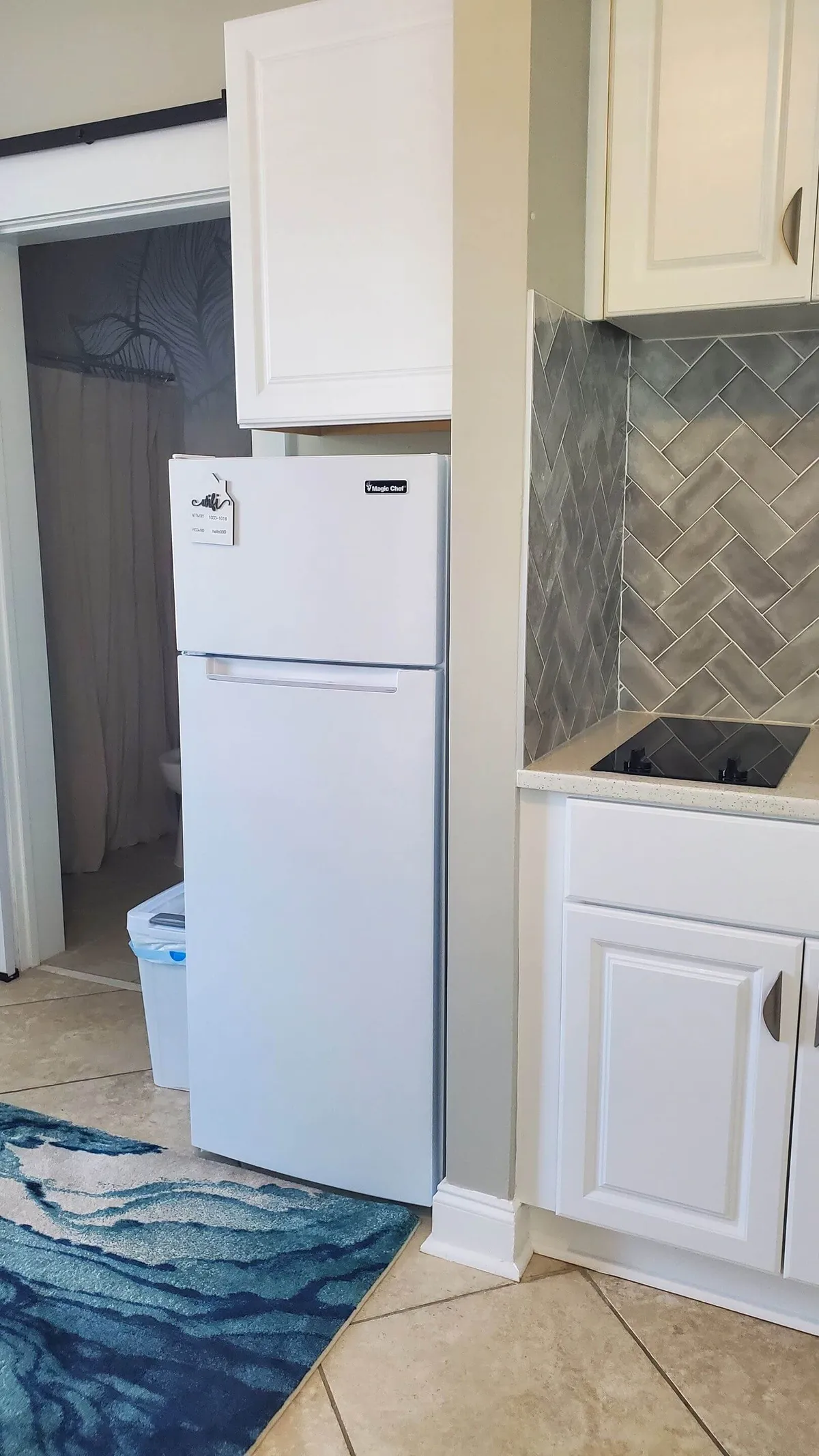 A bright, functional kitchenette featuring a white refrigerator, a blue rug for a pop of color, and a stylish herringbone backsplash. The space is open and ideal for cooking or enjoying casual meals, with enough room for multiple guests to gather.