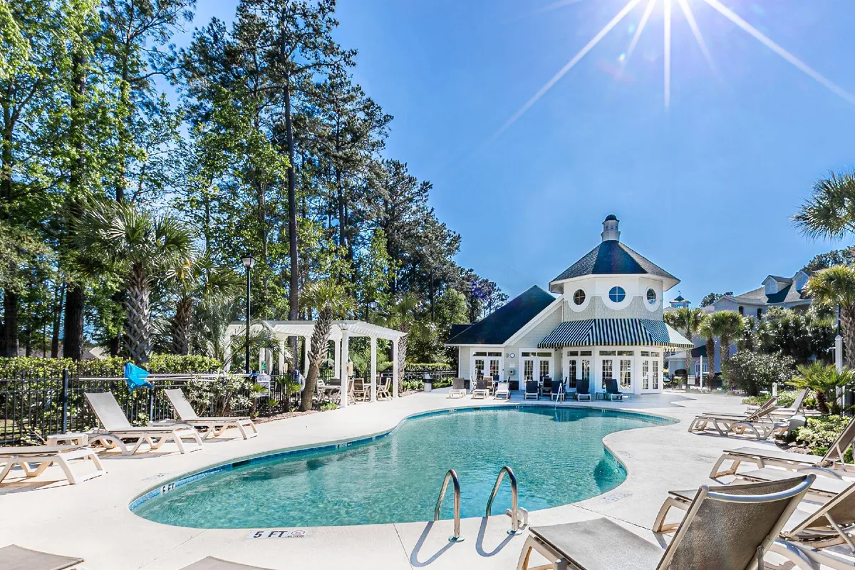 This image features a sparkling swimming pool surrounded by lounge chairs and beautifully landscaped gardens, with the elegant clubhouse in the background. The setting exudes relaxation, offering both sunbathing and swimming opportunities in a resort-like atmosphere.