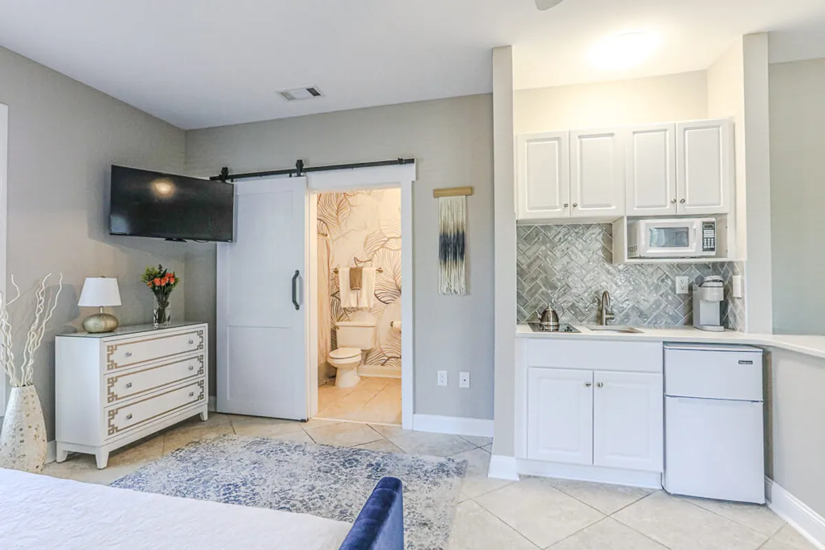 A modern, open-concept studio setup featuring a plush bed, handy kitchenette, and a television. The area is bathed in natural light, suggesting a pleasant, flexible environment perfect for both unwinding and spending quality family time.