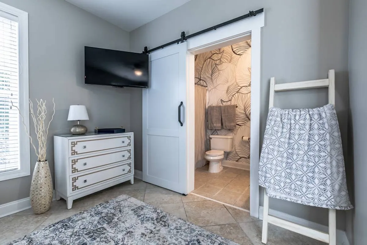 A tranquil, softly lit room with a towel rack displaying plush towels, a white dresser, decorative vase, and a sliding door. The space radiates a calm, serene atmosphere, and though not an explicit bathroom, it offers a glimpse of the relaxation and comfort that extend from the bathroom to adjacent spaces.