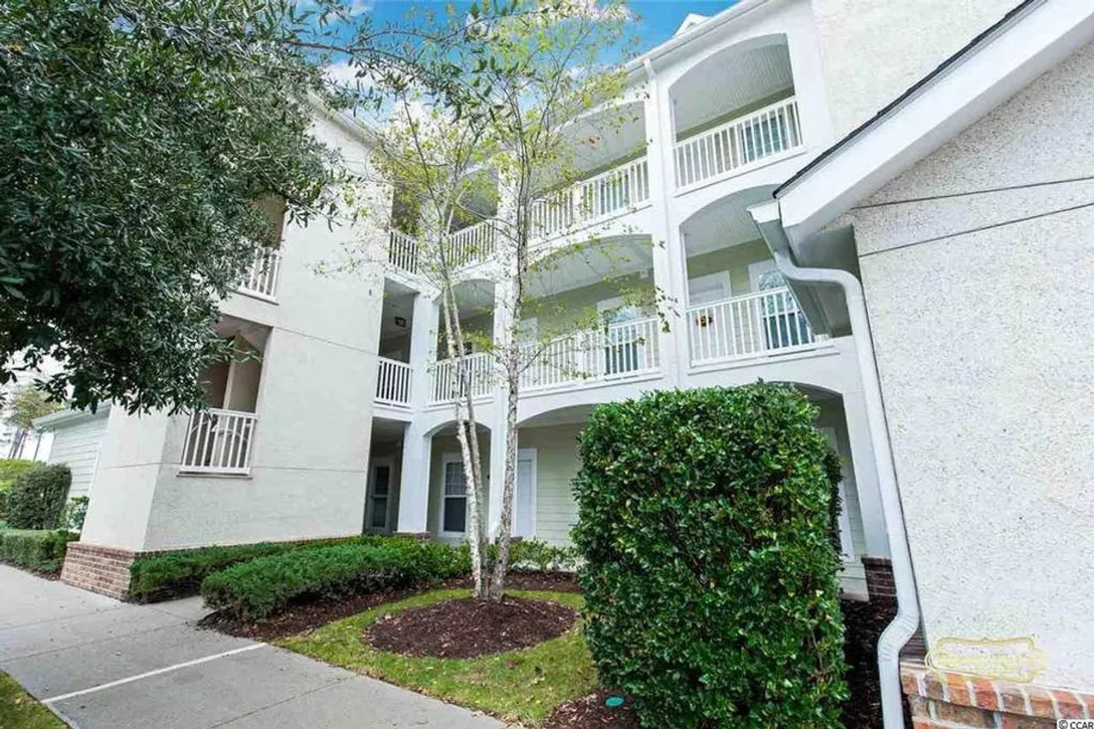 An exterior view of the building with lush greenery, balconies, and a welcoming pathway. The image captures the inviting facade, the presence of outdoor spaces, and the sense of community offered by the property. The scene suggests relaxation on balconies and an enjoyable, serene environment.